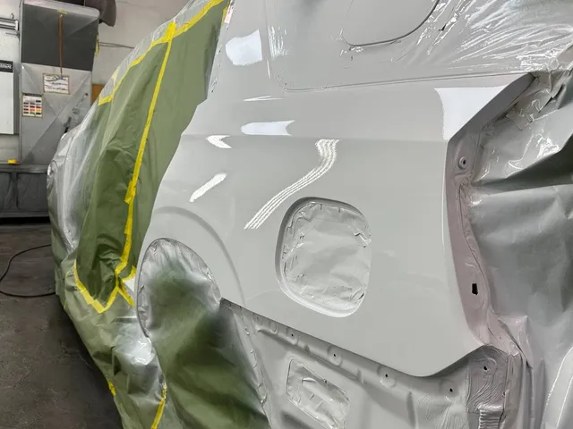 Freshly painted side of a white SUV in the paint booth