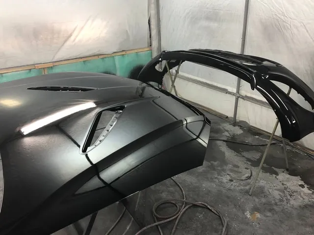 Freshly painted black hood and bumper cover in the paint booth